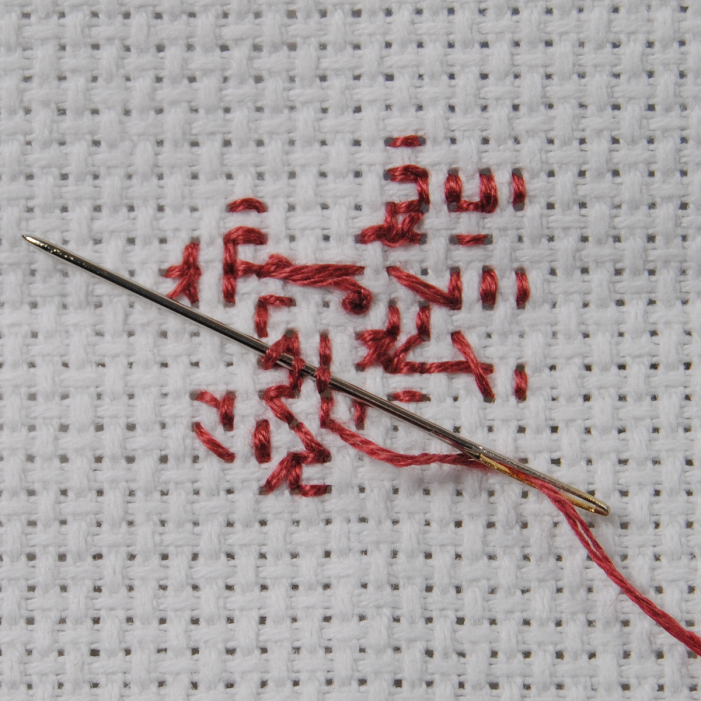 Demonstration of how to tuck the end of your thread behind your cross stitch.