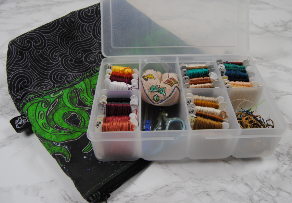 A miniature thread box full with 3 small projects worth of thread, small embroidery scissors, seam ripper, pin cushion, and some orts.