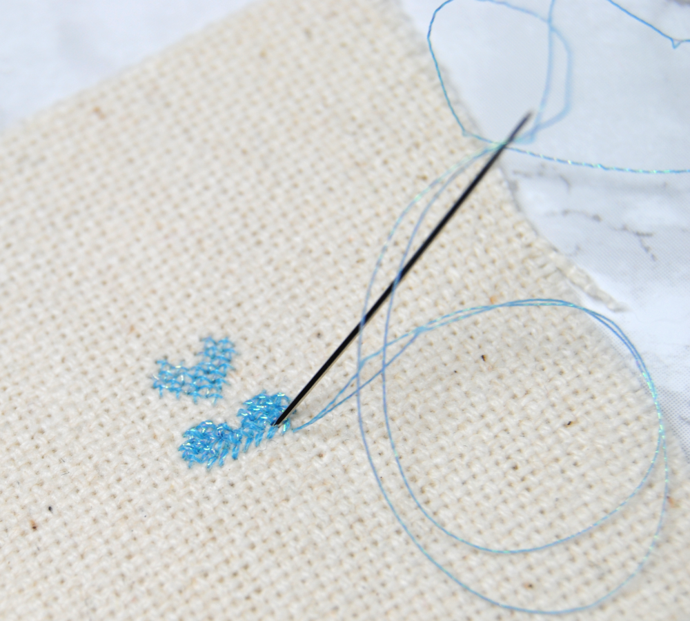 A close up of a partially stitched heart on 28 count fabric using 2 strands over 1
