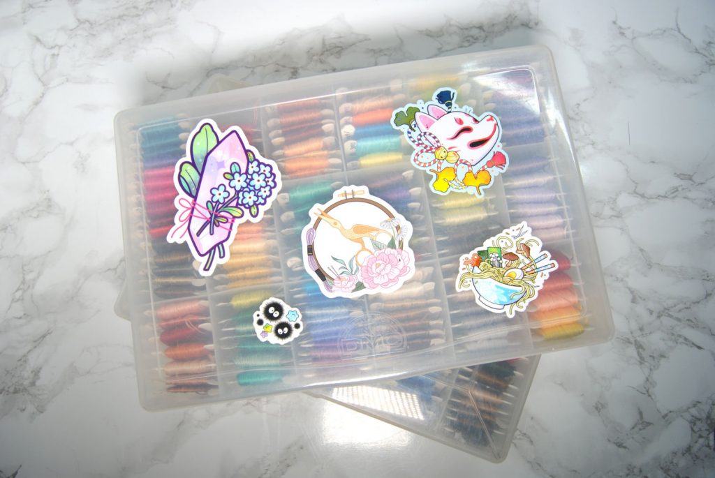 Several Stickers on a floss box. Stickers by StitchingSabbatical and Michelle Coffee