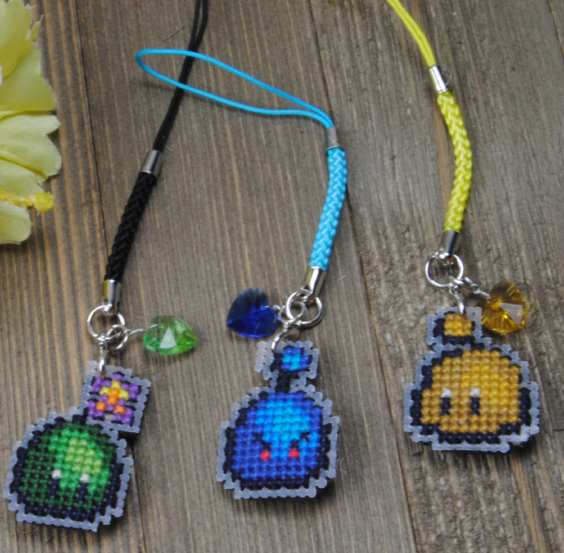 Three cross stitched cell phone fobs with small colored heart charms.