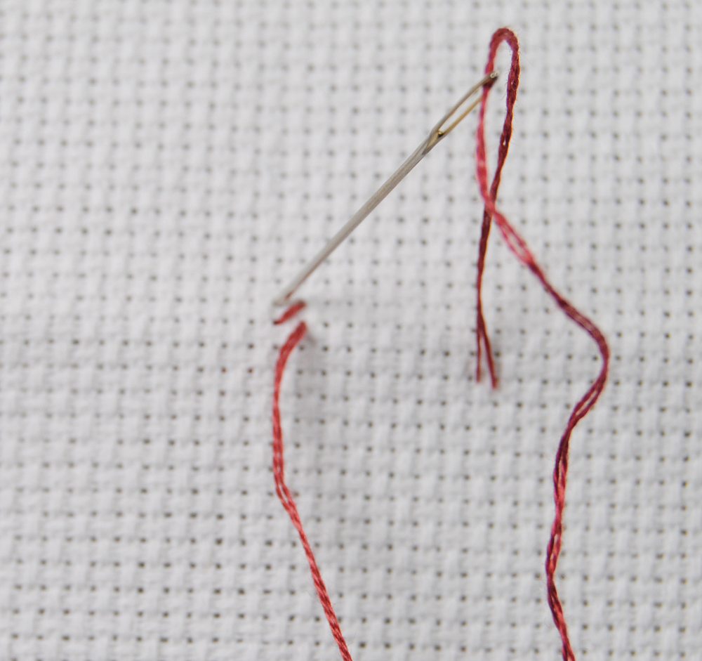 A close up demonstration of how to make a cross stitch.