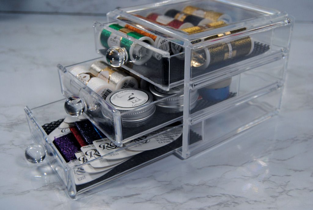 A small set of acrylic drawers holding a variety of metallic threads.