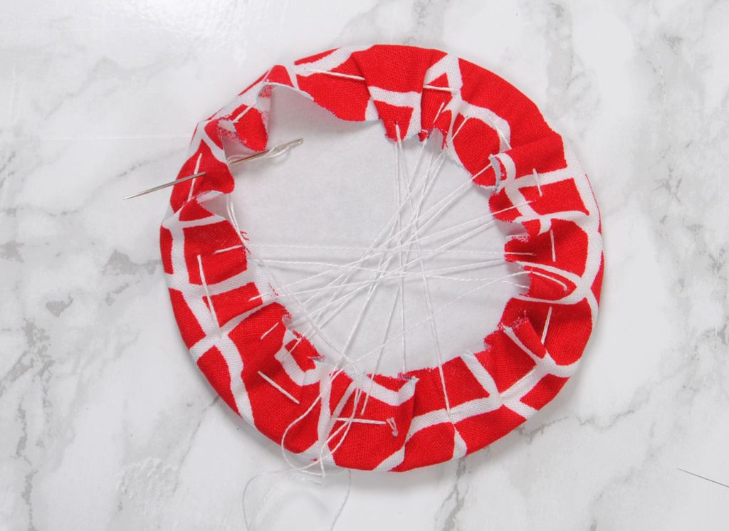 Sewing fabric around a cardboard disc.
