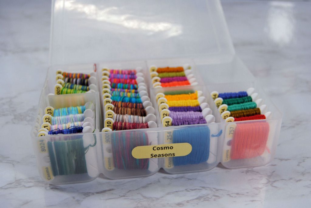 A small plastic box full of Cosmo Seasons thread on bobbins