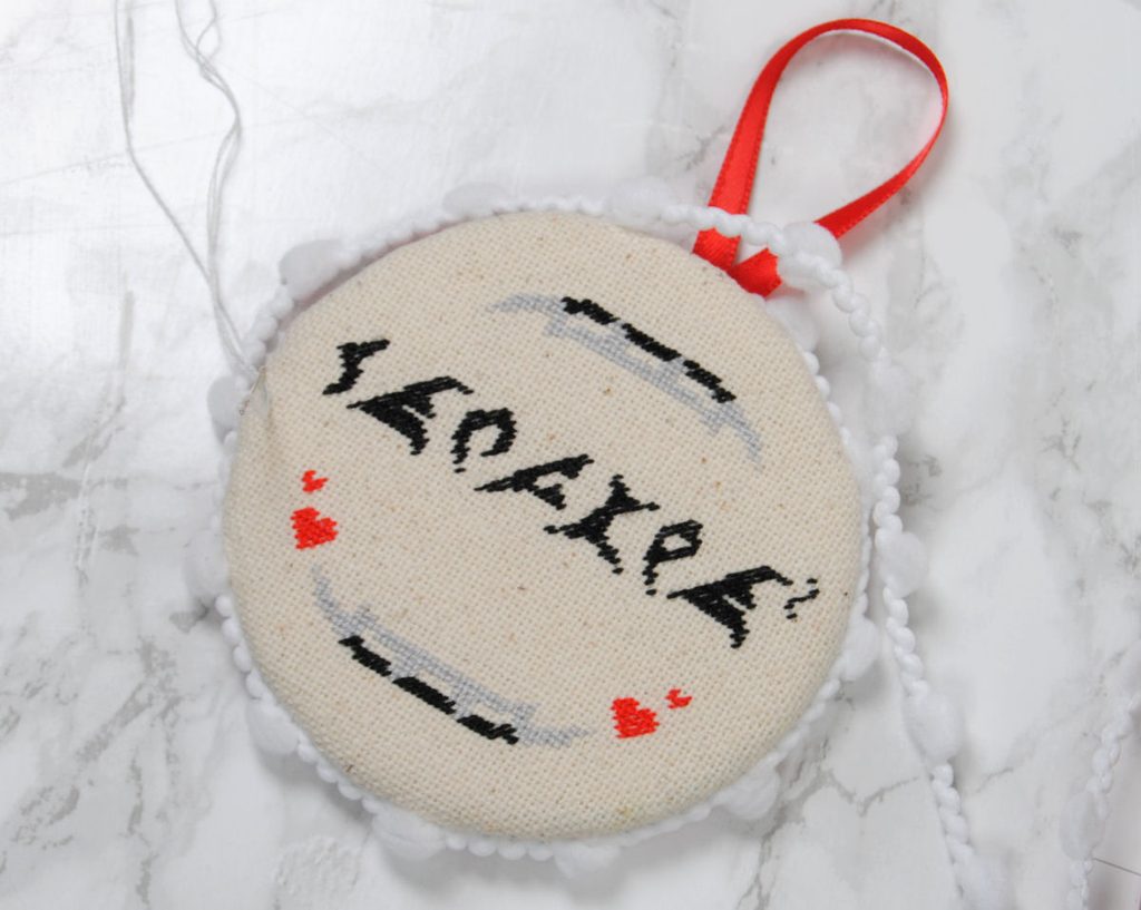 Sewing pom pom edging onto a round ornament.