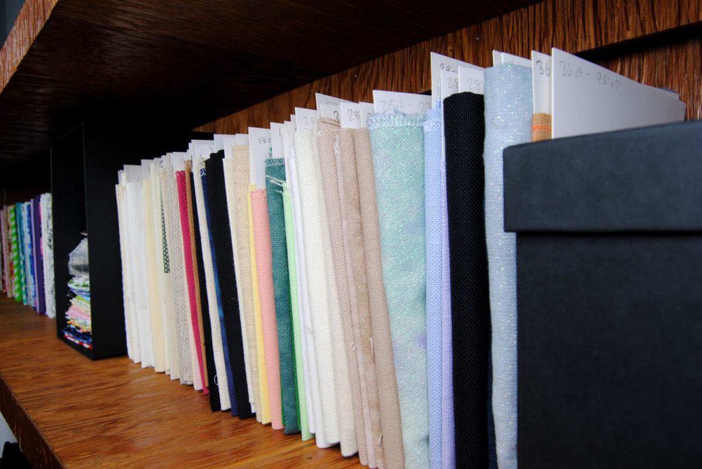 A shelf of cross stitch fabrics on mini bolts.