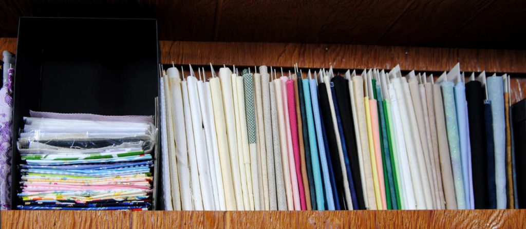 A shelf of aida and evenweave fabrics wrapped on comic book board mini bolts