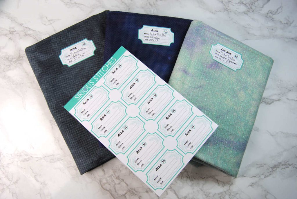 Examples of cross stitch fabric wrapped around comic book board and labeled with a sticker.