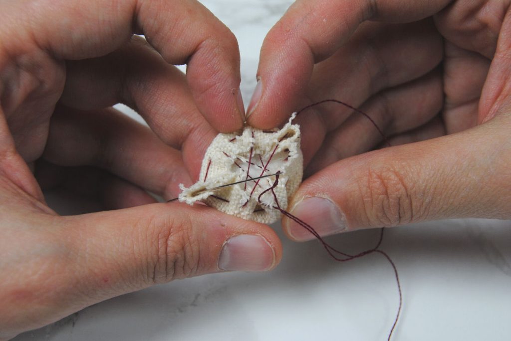 Demonstration of stitching across the fabric to tightly wrap a circle in fabric.