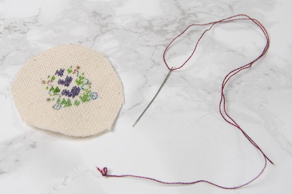 A petite point design trimmed to a small circle in preparation to be made into a pendant.