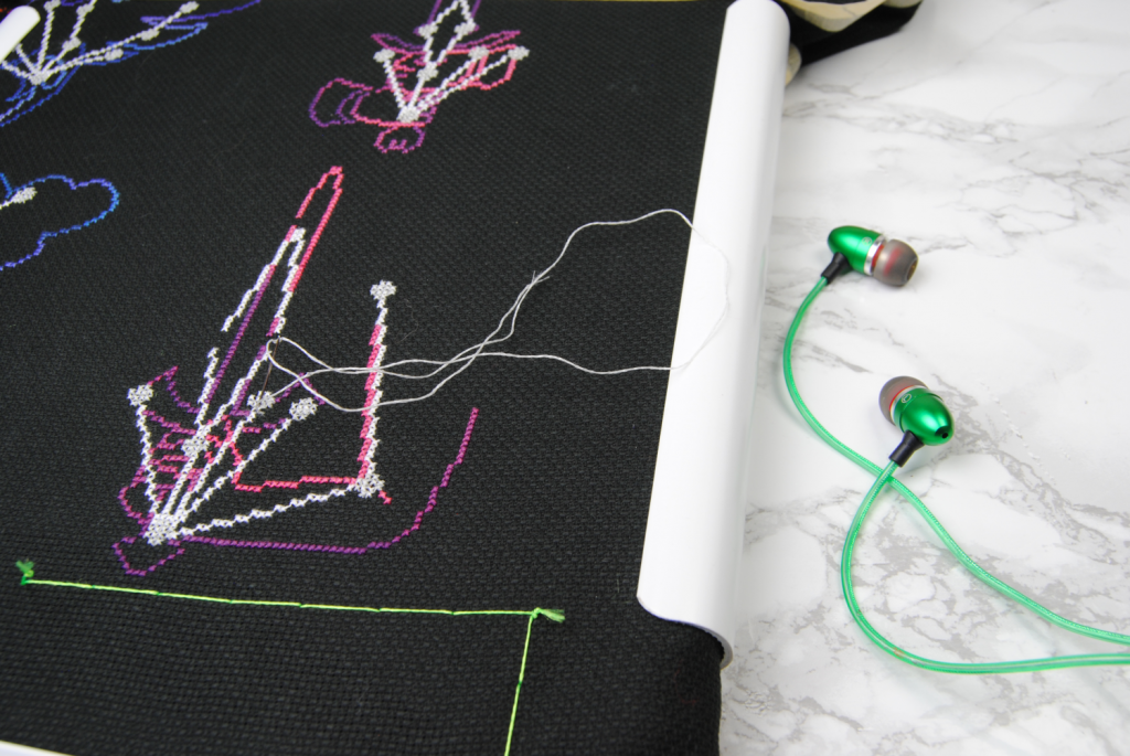 Shot of some earphones next to an in-progress cross stitch project.