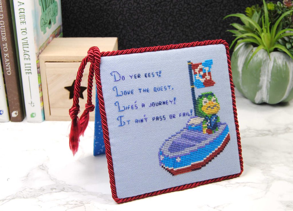 A finished cross stitch of Kapp'n turned into a flatfold that stands on its own.