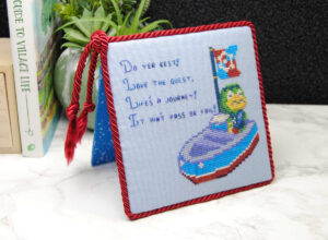 A finished cross stitch of Kapp'n turned into a flatfold that stands on its own.