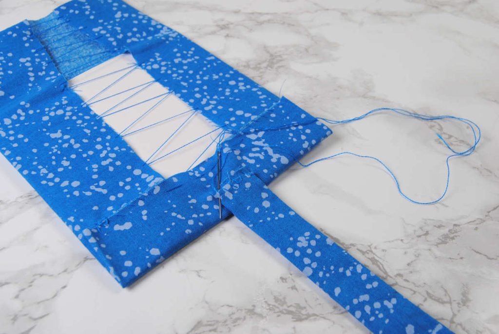 Sewing the long fabric strip to the inner edge of the fabric-covered square with the longer flap.