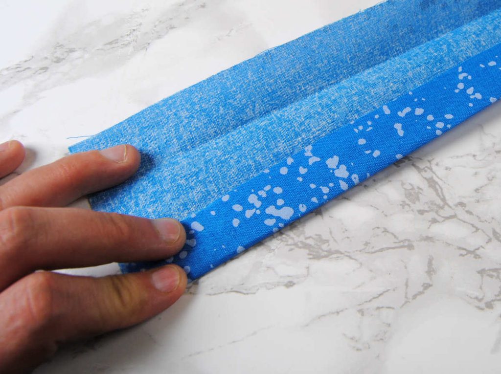 Folding the edges of a long fabric strip into the center to create a tube.