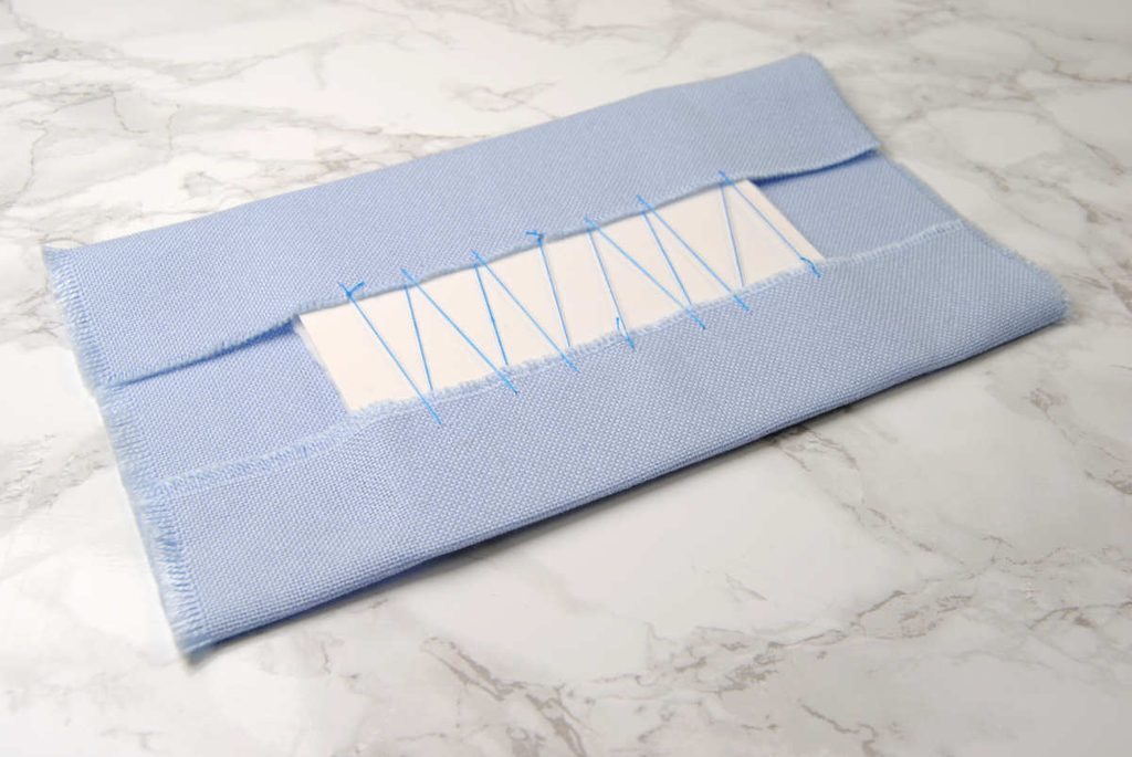 Sewing fabric around cardstock using the lacing method.