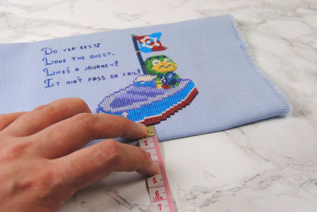 Measuring space around the cross stitch design to ensure it's properly centered.