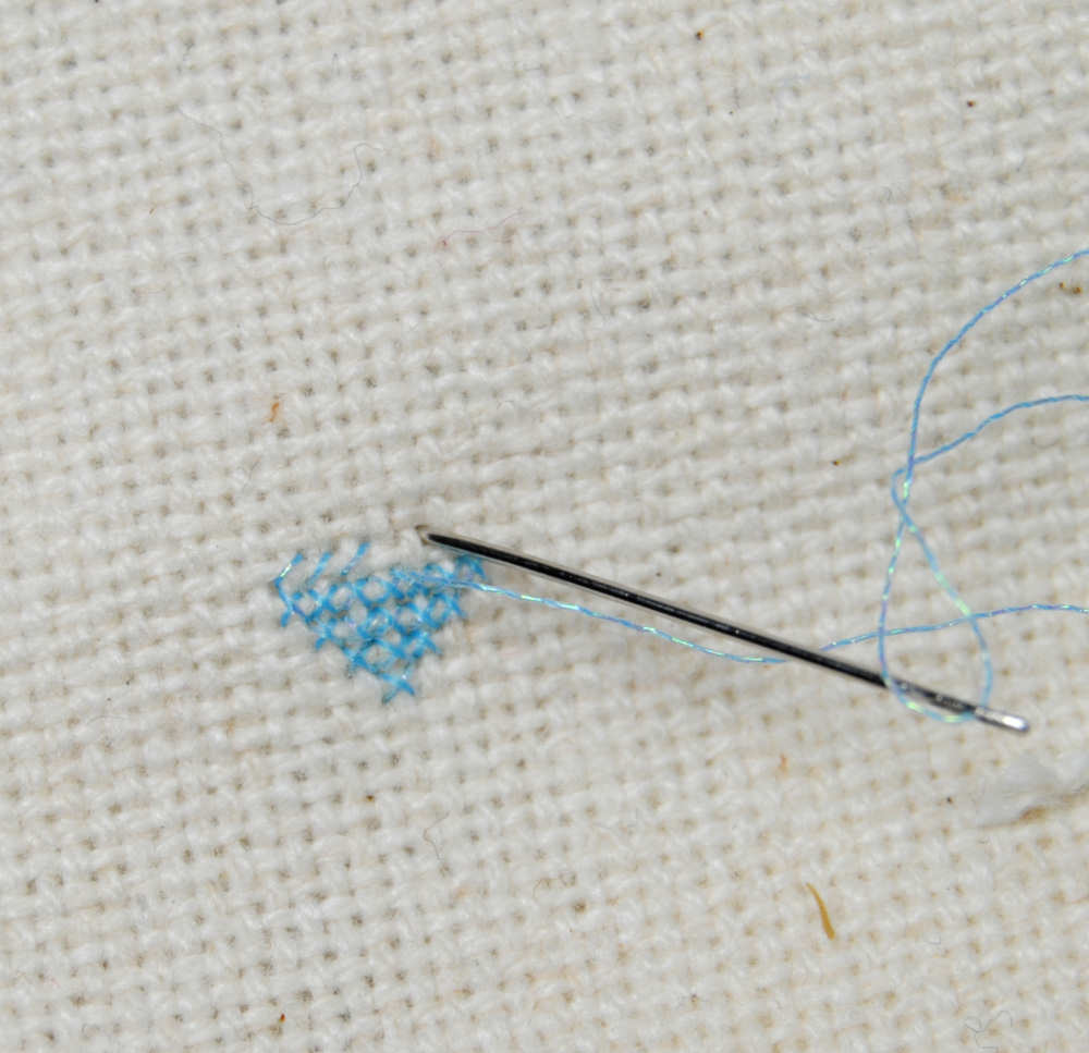 Closeup of a single strand of Sulky metallic cross stitched over 1 on 28 count evenweave.