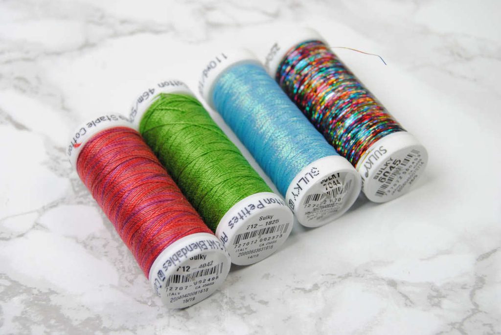 Four spools of varying colors and weights of Sulky thread.