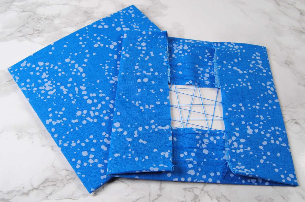 Two squares of cardstock with fabric wrapped around it and sewn in place.