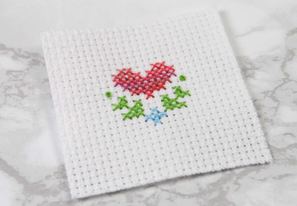 An unfinished cross stitch of a heart done in Sulky threads.