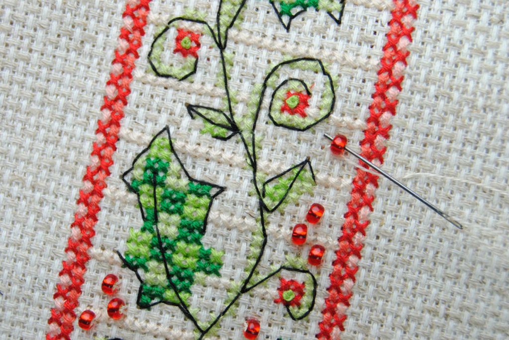 Close up of a bead being cross stitched onto aida fabric.