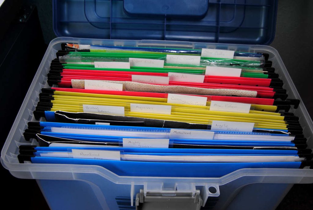Closeup of a plastic hanging file folder bin being used to store cross stitch patterns and materials.