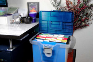 A plastic bin for hanging file folders being used to store cross stitch patterns, wips, and materials.