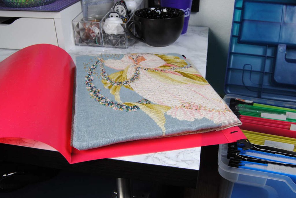 A finished Lavender & Lace cross stitch stored in a hanging file folder.