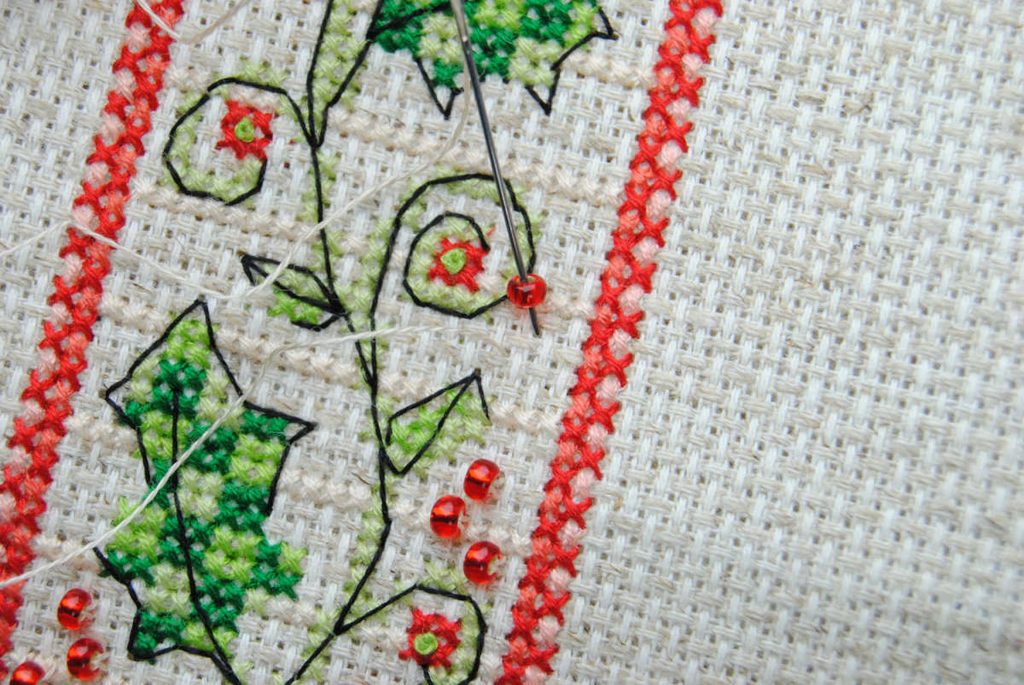 Close up of a beginning a cross stitch with a bead on the needle.