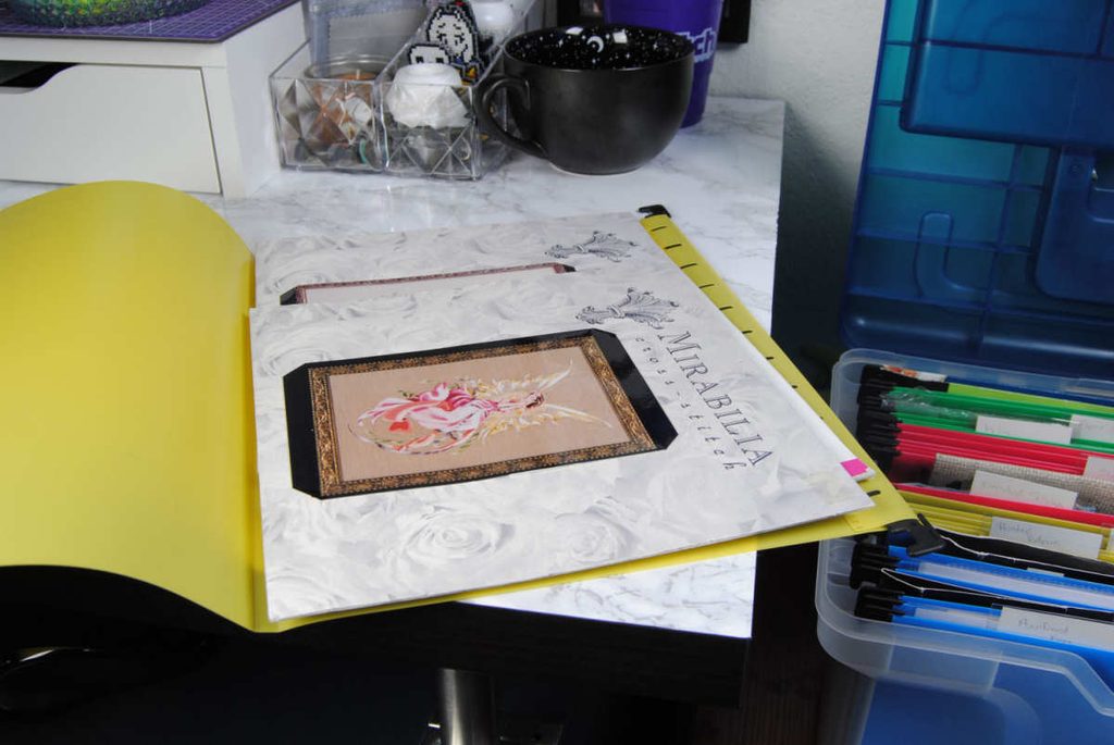 Mirabilia cross stitch patterns stored in a hanging file folder.
