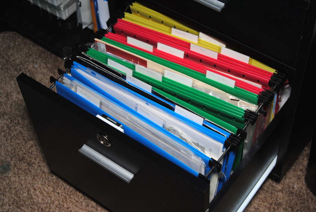 A low printer stand with a file cabinet drawer being used to store cross stitch patterns, wips, and materials.