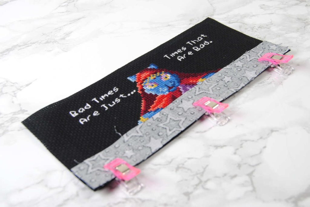 Clipping a strip of fabric to the front of a cross stitch panel.