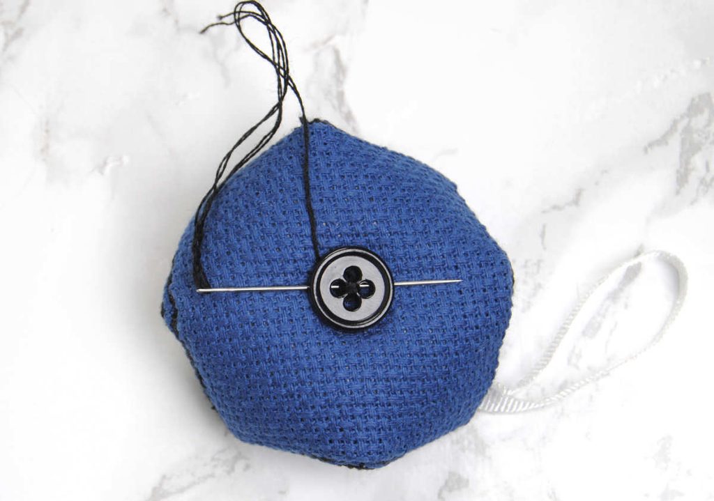 Demonstrating securing a button to the back of a biscornu.