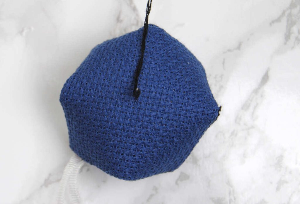 Demonstrating cinching the center of a biscornu with thread.