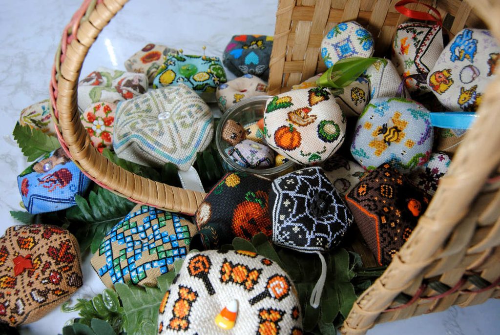 Examples of cross stitched biscornu in all different sizes, themes, and colors.