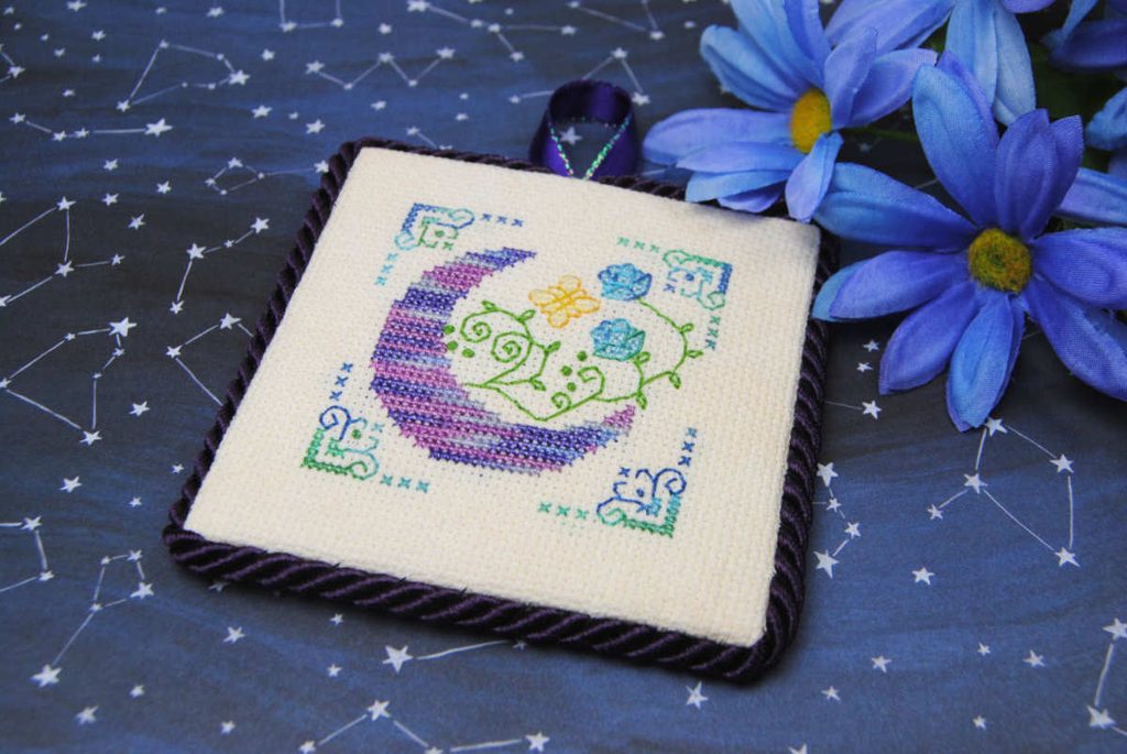 A cross stitch ornament featuring a moon and flowers stitched with Sulky Petites and Blendables.