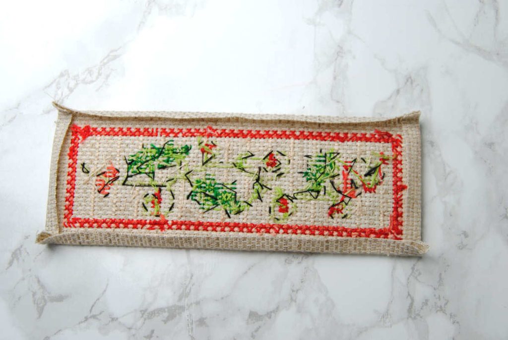 Demonstrating folding in the edges of a finished cross stitch.