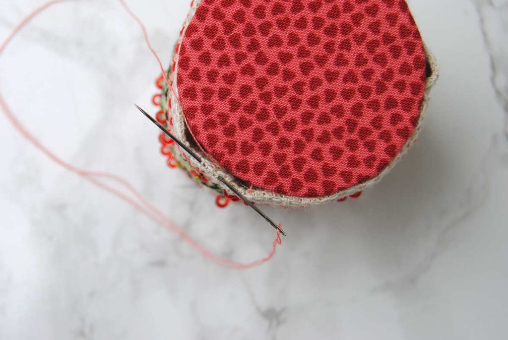 Demonstrating the ladder stitch while sewing the bottom of a pin drum on.