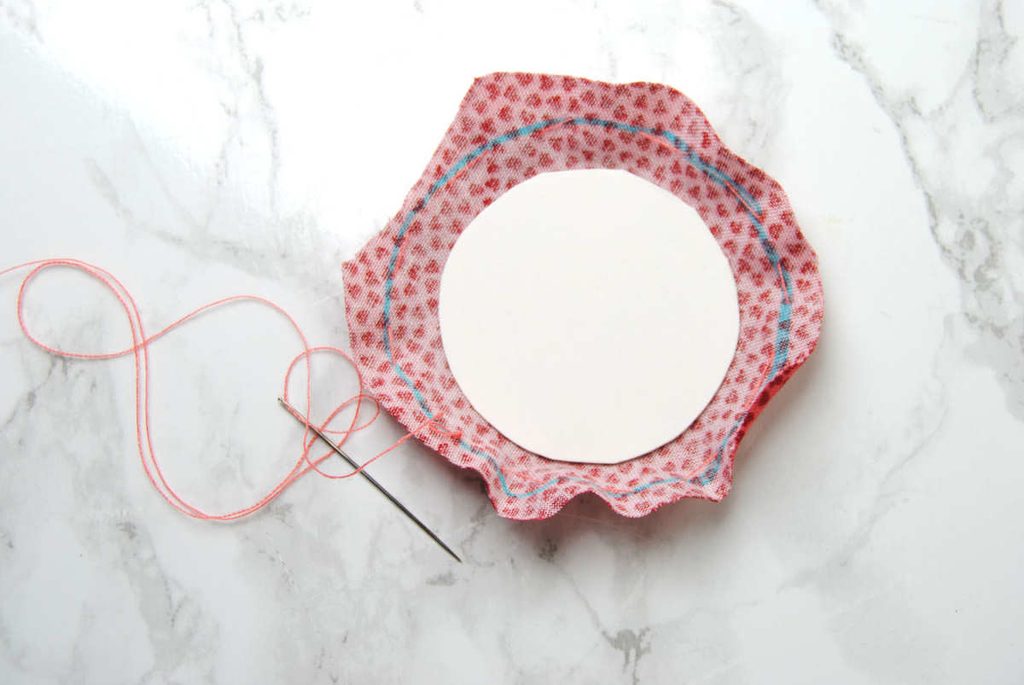 Demonstrating a running stitch run around the edges of a fabric circle