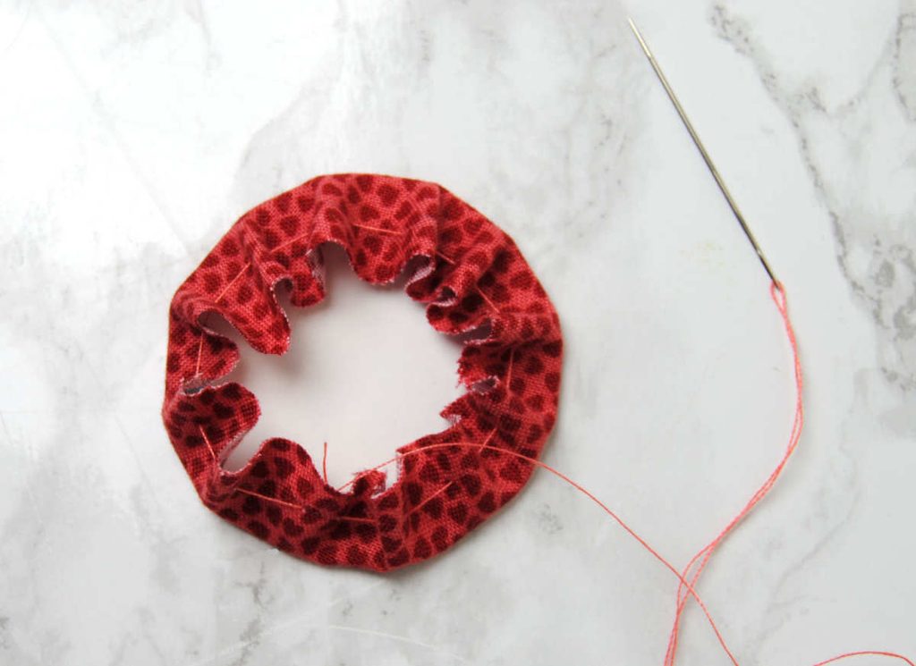 A fabric circle being inched around a cardstock circle by pulling a running stitch tight.