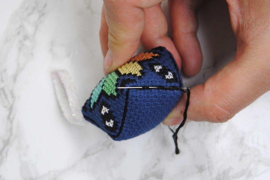 Demonstrating securing the tail of your thread in the edges of the biscornu.