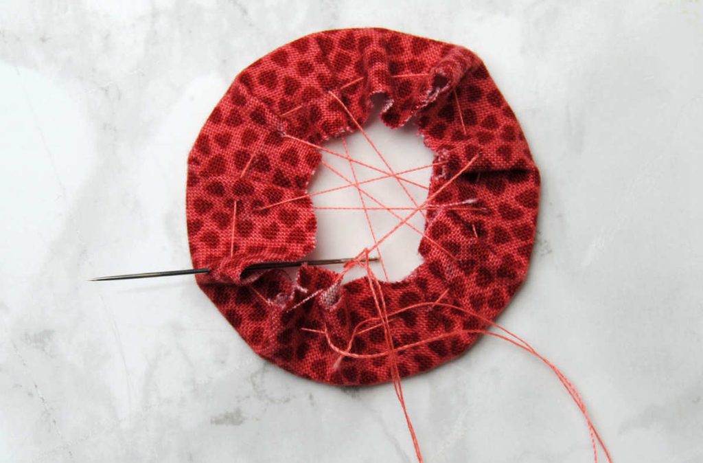 Fabric wrapped around a cardstock circle being sewn across to secure it in place.