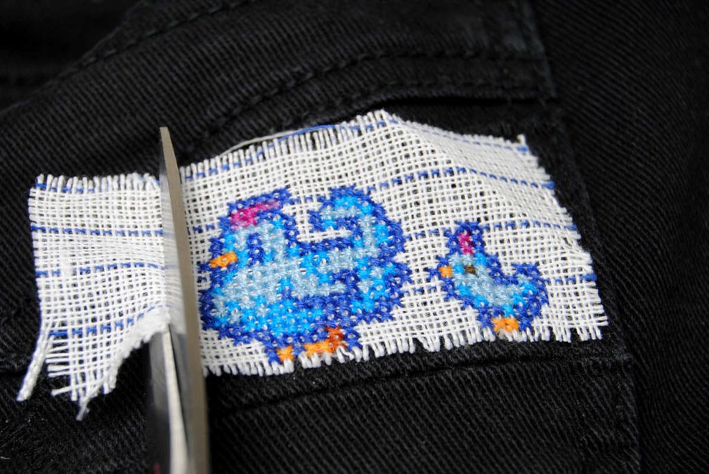 Trimming waste canvas close to the finished cross stitch.