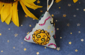 A completed cross stitch humbug ornament featuring summer motifs.