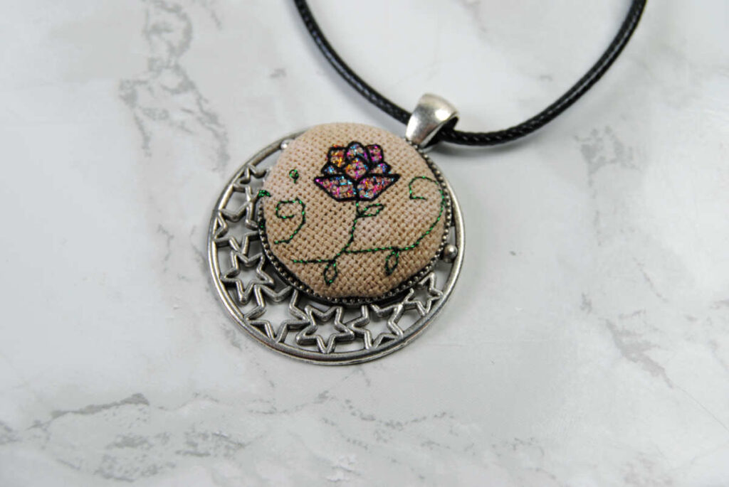 Cross stitch necklace pendant featuring a lotus flower in a moon pendant tray.