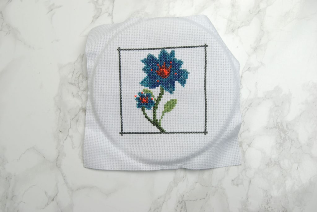 A finished cross stitch project, complete with heavy hoop rings that could use washing out.