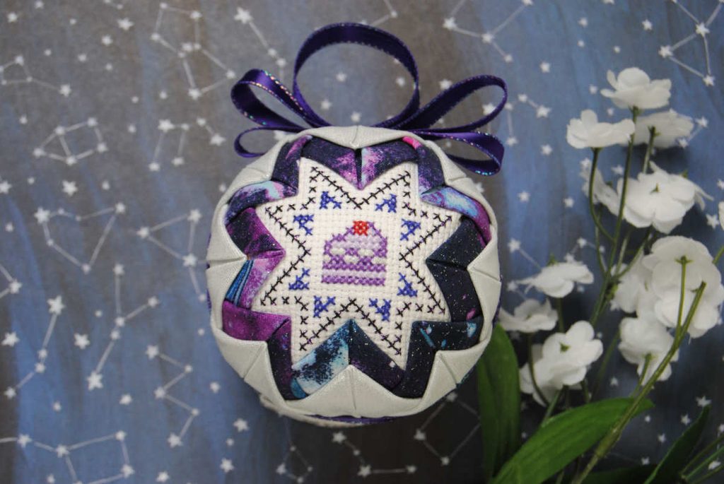 A traditional quilted ornament with a cross stitch cake center panel.