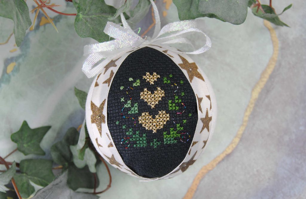 Staged shot of a cross stitch fabric ornament, complete with ribbon topper.